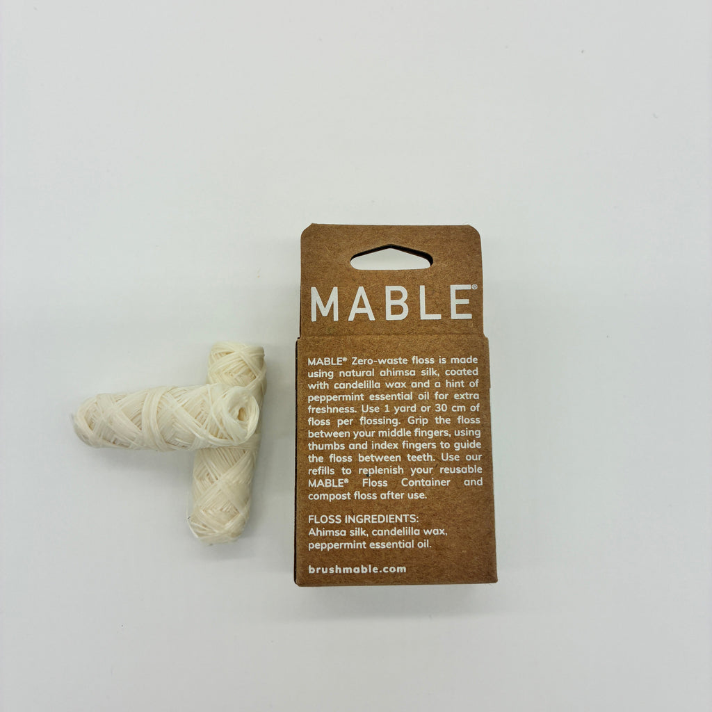 Mable zero-waste floss in a brown cardboard package with a small bundle of off-white wound cotton thread next to it, photographed on a plain white background.