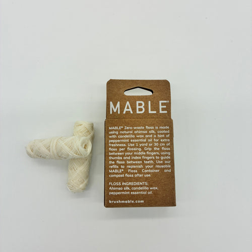 Mable zero-waste floss in a brown cardboard package with a small bundle of off-white wound cotton thread next to it, photographed on a plain white background.