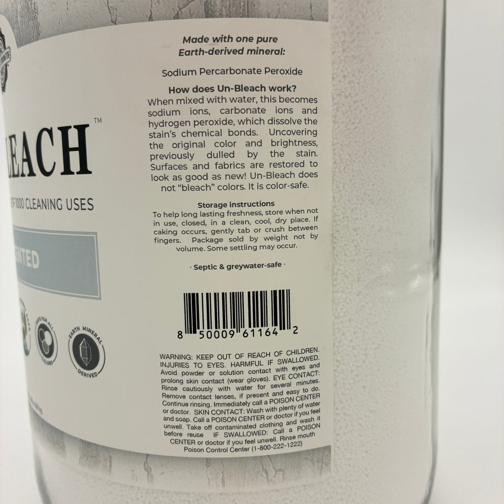A close-up of the back label of a large white glass bottle of Un-Bleach cleaning powder, showing product details, instructions, and a barcode.
